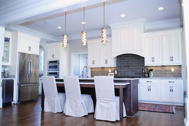 Mid-sized transitional l-shaped medium tone wood floor eat-in kitchen photo in Birmingham with a farmhouse sink, shaker cabinets, white cabinets, granite countertops, gray backsplash, porcelain backsplash, stainless steel appliances and an island