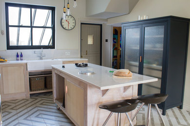Eat-in kitchen - mid-sized eclectic l-shaped ceramic tile and beige floor eat-in kitchen idea in Manchester with a farmhouse sink, flat-panel cabinets, light wood cabinets, solid surface countertops, colored appliances and an island