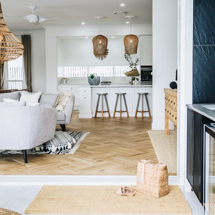 Small traditional galley open plan kitchen in Brisbane with a double-bowl sink, recessed-panel cabinets, white cabinets, quartz benchtops, white splashback, black appliances, medium hardwood floors, with island, brown floor and beige benchtop.