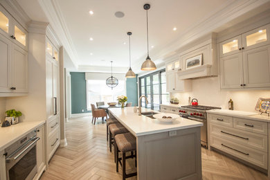 Example of a large transitional galley ceramic tile eat-in kitchen design in Toronto with a double-bowl sink, shaker cabinets, white cabinets, quartzite countertops, white backsplash, ceramic backsplash, stainless steel appliances and an island