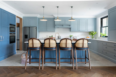 Inspiration for a large beach style u-shaped kitchen in Surrey with blue cabinets, quartz worktops, stainless steel appliances, ceramic flooring, an island, white worktops, shaker cabinets, white splashback and grey floors.