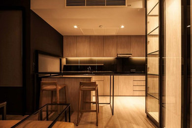 Example of a mid-sized minimalist single-wall light wood floor open concept kitchen design in New York with an undermount sink, flat-panel cabinets, light wood cabinets, solid surface countertops, black backsplash, glass sheet backsplash, paneled appliances and a peninsula