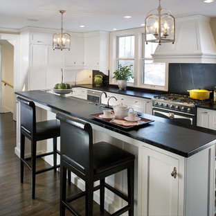 Esempio di una grande cucina a L chic con ante con riquadro incassato, ante bianche, top in saponaria, paraspruzzi nero, paraspruzzi in lastra di pietra, elettrodomestici neri, parquet scuro e isola