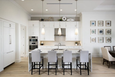 Beach style light wood floor kitchen photo in Miami with a triple-bowl sink, shaker cabinets, white cabinets, quartzite countertops, gray backsplash, glass tile backsplash, stainless steel appliances and an island