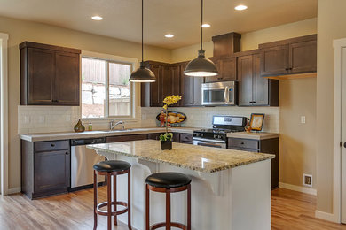 Open concept kitchen - mid-sized transitional l-shaped open concept kitchen idea in Portland with an undermount sink, shaker cabinets, dark wood cabinets, granite countertops, white backsplash, subway tile backsplash, stainless steel appliances and an island