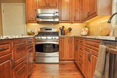 Inspiration for a mid-sized transitional medium tone wood floor kitchen remodel in Boise with an undermount sink, raised-panel cabinets, medium tone wood cabinets, granite countertops, beige backsplash, porcelain backsplash, stainless steel appliances and an island