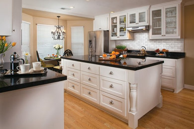 Eat-in kitchen - mid-sized transitional u-shaped medium tone wood floor and brown floor eat-in kitchen idea in New Orleans with a single-bowl sink, shaker cabinets, white cabinets, solid surface countertops, white backsplash, stainless steel appliances and an island