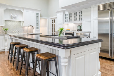 Large transitional l-shaped dark wood floor and brown floor open concept kitchen photo in Bridgeport with a farmhouse sink, beaded inset cabinets, white cabinets, wood countertops, beige backsplash, glass tile backsplash, stainless steel appliances and an island