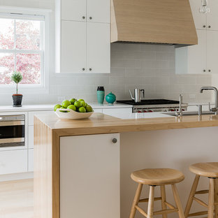 Inspiration for a mid-sized scandinavian galley light wood floor eat-in kitchen remodel in Boston with an undermount sink, flat-panel cabinets, white cabinets, gray backsplash, wood countertops, stainless steel appliances and ceramic backsplash
