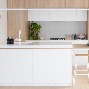 Design ideas for a contemporary galley kitchen in Melbourne with an integrated sink, flat-panel cabinets, light wood cabinets, white splashback, matchstick tile splashback, panelled appliances, light hardwood floors, a peninsula, white benchtop and beige floor.