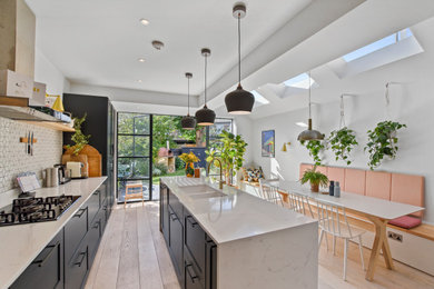 Small scandi galley kitchen/diner in London with an integrated sink, shaker cabinets, blue cabinets, light hardwood flooring, an island and white worktops.