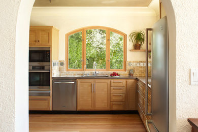 Example of a mid-sized classic l-shaped medium tone wood floor and brown floor enclosed kitchen design in San Francisco with a double-bowl sink, shaker cabinets, medium tone wood cabinets, beige backsplash, ceramic backsplash, stainless steel appliances and no island
