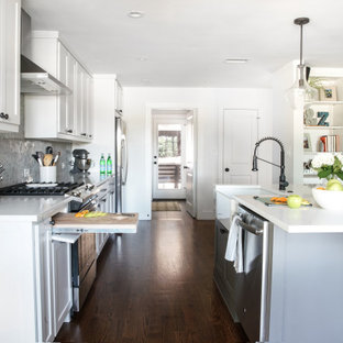 Small midcentury single-wall eat-in kitchen in Dallas with a farmhouse sink, flat-panel cabinets, white cabinets, granite benchtops, grey splashback, granite splashback, black appliances, dark hardwood floors, with island, brown floor and white benchtop.