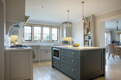 Photo of a large classic u-shaped kitchen/diner in Gloucestershire with a double-bowl sink, shaker cabinets, blue cabinets, granite worktops, white splashback, glass sheet splashback, stainless steel appliances, travertine flooring, an island, beige floors and white worktops.