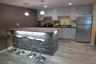 Eat-in kitchen - mid-sized eclectic single-wall porcelain tile and gray floor eat-in kitchen idea in Chicago with a drop-in sink, shaker cabinets, white cabinets, stainless steel appliances, an island, soapstone countertops, black backsplash and stone slab backsplash