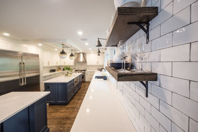 Example of a large transitional u-shaped medium tone wood floor and brown floor eat-in kitchen design in Toronto with an undermount sink, shaker cabinets, white cabinets, solid surface countertops, white backsplash, subway tile backsplash, stainless steel appliances and two islands