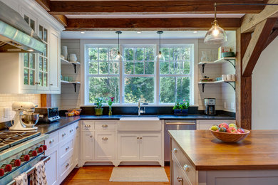 Example of a mid-sized country l-shaped medium tone wood floor kitchen design in Burlington with a farmhouse sink, white cabinets, soapstone countertops, stainless steel appliances, an island, shaker cabinets, white backsplash and subway tile backsplash