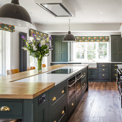 Example of a large transitional u-shaped medium tone wood floor and brown floor kitchen design in Manchester with shaker cabinets, green cabinets, granite countertops, white backsplash, limestone backsplash, an island, white countertops and a farmhouse sink