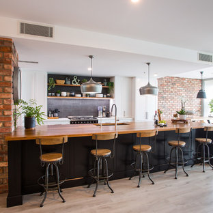 Expansive industrial galley eat-in kitchen in Brisbane with a double-bowl sink, recessed-panel cabinets, black cabinets, wood benchtops, black splashback, subway tile splashback, black appliances, with island, grey floor and white benchtop.