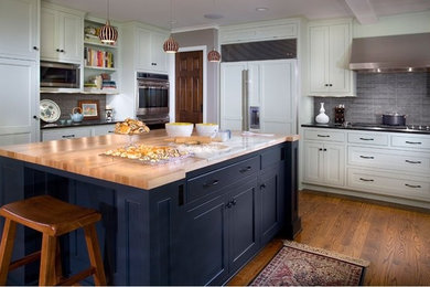 This is an example of a large traditional u-shaped kitchen/diner in Minneapolis with shaker cabinets, white cabinets, an island, wood worktops, grey splashback, ceramic splashback, stainless steel appliances and medium hardwood flooring.