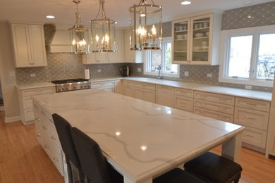Inspiration for a large transitional l-shaped light wood floor open concept kitchen remodel in Chicago with an undermount sink, recessed-panel cabinets, white cabinets, quartz countertops, gray backsplash, ceramic backsplash, paneled appliances and an island