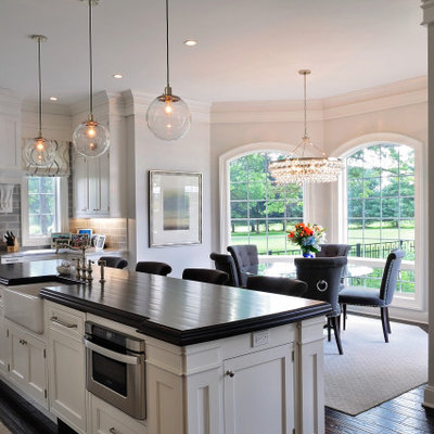 Mid-sized elegant l-shaped dark wood floor and brown floor eat-in kitchen photo in Philadelphia with a farmhouse sink, recessed-panel cabinets, white cabinets, granite countertops, gray backsplash, subway tile backsplash, paneled appliances, an island and gray countertops