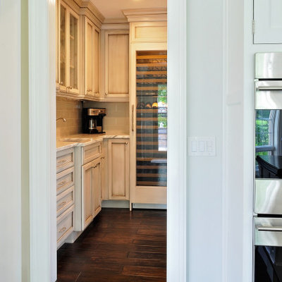Example of a mid-sized classic l-shaped dark wood floor and brown floor eat-in kitchen design in Philadelphia with a farmhouse sink, recessed-panel cabinets, white cabinets, granite countertops, gray backsplash, subway tile backsplash, paneled appliances, an island and gray countertops