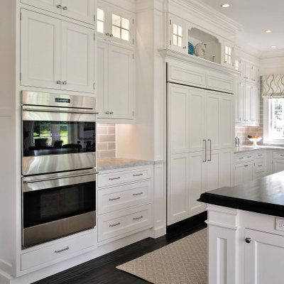 Inspiration for a mid-sized timeless l-shaped dark wood floor and brown floor eat-in kitchen remodel in Philadelphia with a farmhouse sink, recessed-panel cabinets, white cabinets, granite countertops, gray backsplash, subway tile backsplash, paneled appliances, an island and gray countertops