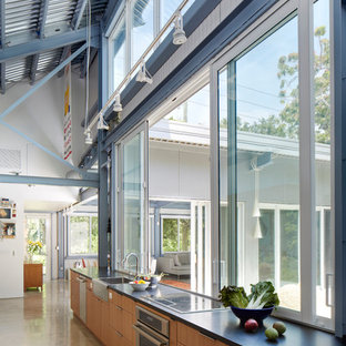 Large industrial eat-in kitchen photos - Large urban single-wall concrete floor eat-in kitchen photo in Miami with flat-panel cabinets, light wood cabinets, stainless steel appliances, no island, a farmhouse sink and solid surface countertops