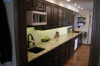 Inspiration for a mid-sized transitional l-shaped medium tone wood floor eat-in kitchen remodel in Boise with an undermount sink, raised-panel cabinets, dark wood cabinets, granite countertops, white backsplash, subway tile backsplash, white appliances and no island