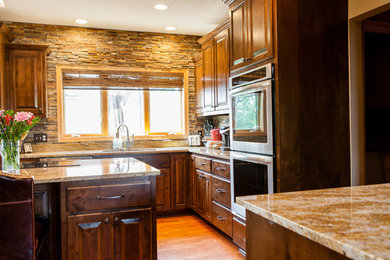 Example of a mid-sized transitional l-shaped light wood floor eat-in kitchen design in Minneapolis with an undermount sink, raised-panel cabinets, medium tone wood cabinets, granite countertops, brown backsplash, stone tile backsplash, stainless steel appliances and an island