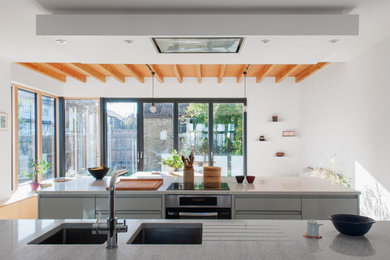ロンドンにある高級な中くらいなコンテンポラリースタイルのおしゃれなマルチアイランドキッチン (一体型シンク、フラットパネル扉のキャビネット、グレーのキャビネット、パネルと同色の調理設備、無垢フローリング、グレーのキッチンカウンター) の写真