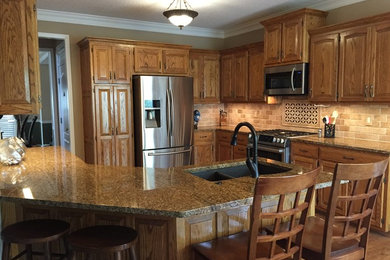 Example of a mid-sized trendy u-shaped medium tone wood floor eat-in kitchen design in Kansas City with an undermount sink, medium tone wood cabinets, beige backsplash, a peninsula, raised-panel cabinets, granite countertops, stone tile backsplash and stainless steel appliances