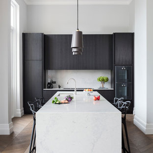 Inspiration for a mid-sized contemporary single-wall eat-in kitchen in London with flat-panel cabinets, dark wood cabinets, medium hardwood floors, brown floor, black appliances, an integrated sink, solid surface benchtops, stone slab splashback and a peninsula.