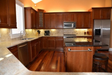 Example of a large transitional galley medium tone wood floor and brown floor open concept kitchen design in Detroit with a double-bowl sink, medium tone wood cabinets, granite countertops, white backsplash, stainless steel appliances and an island