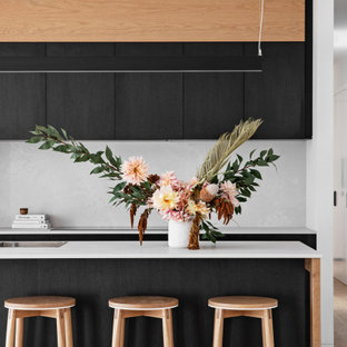 Inspiration for a modern galley kitchen in Wollongong with a drop-in sink, flat-panel cabinets, black cabinets, white splashback, stone slab splashback, stainless steel appliances, medium hardwood floors, with island, brown floor and white benchtop.
