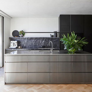 Contemporary l-shaped kitchen in Melbourne with flat-panel cabinets, black cabinets, grey splashback, stone slab splashback, black appliances, light hardwood floors, with island, beige floor and grey benchtop.