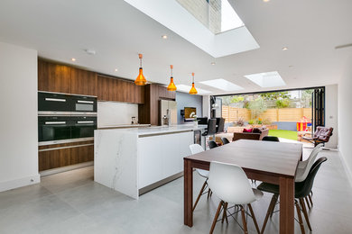 Photo of a contemporary galley open plan kitchen in London with flat-panel cabinets, dark wood cabinets, white splashback, black appliances and an island.