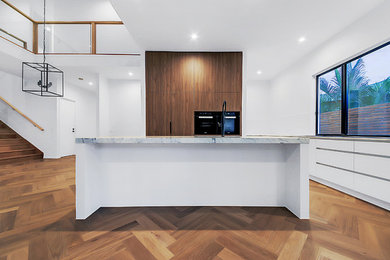 Idéer för funkis linjära vitt kök med öppen planlösning, med en undermonterad diskho, släta luckor, skåp i mellenmörkt trä, marmorbänkskiva, vitt stänkskydd, stänkskydd i porslinskakel, integrerade vitvaror, ljust trägolv, en köksö och beiget golv