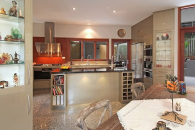 Inspiration för stora moderna kök, med släta luckor, beige skåp, orange stänkskydd, glaspanel som stänkskydd, rostfria vitvaror, betonggolv, en köksö och marmorbänkskiva