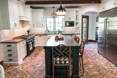 Eat-in kitchen - mid-sized farmhouse u-shaped brick floor and red floor eat-in kitchen idea in Philadelphia with a farmhouse sink, recessed-panel cabinets, white cabinets, soapstone countertops, white backsplash, subway tile backsplash, stainless steel appliances, an island and black countertops