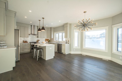 Inspiration for a large contemporary u-shaped open plan kitchen in Calgary with an island, shaker cabinets, grey cabinets, a submerged sink, engineered stone countertops, white splashback, ceramic splashback, stainless steel appliances, dark hardwood flooring and brown floors.