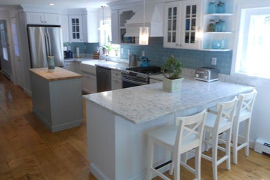 Inspiration for a large coastal u-shaped medium tone wood floor eat-in kitchen remodel in Portland Maine with a farmhouse sink, louvered cabinets, white cabinets, marble countertops, blue backsplash, subway tile backsplash, stainless steel appliances and an island