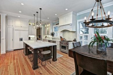 Example of a large trendy l-shaped light wood floor and beige floor eat-in kitchen design in Charleston with an island, raised-panel cabinets, white cabinets, white backsplash, stainless steel appliances, quartzite countertops, glass tile backsplash and a farmhouse sink