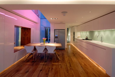 ロンドンにある高級な中くらいなコンテンポラリースタイルのおしゃれなキッチン (一体型シンク、フラットパネル扉のキャビネット、白いキャビネット、人工大理石カウンター、緑のキッチンパネル、ガラス板のキッチンパネル、パネルと同色の調理設備、淡色無垢フローリング、アイランドなし) の写真