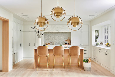This is an example of a medium sized contemporary u-shaped open plan kitchen in Vancouver with a submerged sink, flat-panel cabinets, white cabinets, marble worktops, white splashback, marble splashback, integrated appliances, medium hardwood flooring, an island, beige floors and white worktops.