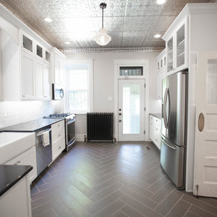 This is an example of a mid-sized traditional u-shaped separate kitchen in St Louis with a farmhouse sink, shaker cabinets, white cabinets, stone tile splashback, granite benchtops, white splashback, stainless steel appliances, vinyl floors and no island.