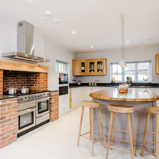 Photo of a large rural u-shaped enclosed kitchen in Essex with a submerged sink, recessed-panel cabinets, beige cabinets, granite worktops, orange splashback, brick splashback, stainless steel appliances, an island, grey floors and black worktops.