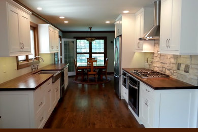 Inspiration for a farmhouse galley medium tone wood floor eat-in kitchen remodel in Chicago with a farmhouse sink, shaker cabinets, white cabinets, wood countertops, beige backsplash, stone tile backsplash, stainless steel appliances and no island
