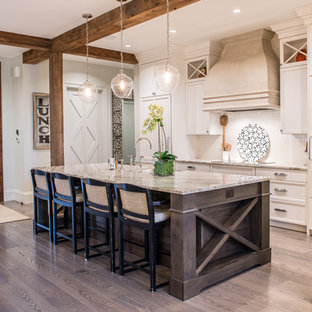 Modelo de cocina de galera, rústica, con armarios con paneles empotrados, puertas de armario beige, salpicadero blanco, salpicadero de azulejos tipo metro, una isla, fregadero sobremueble, electrodomésticos blancos y suelo de madera clara